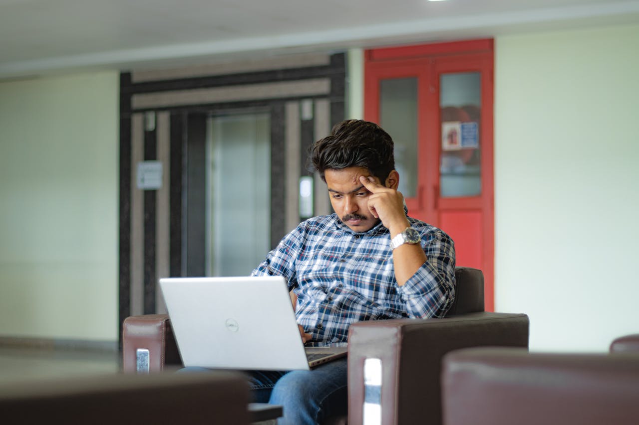 Man in plaid shirt concentrating on laptop work in a modern indoor setting.